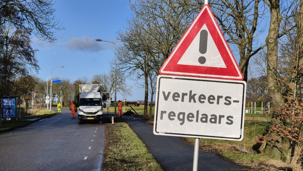Nathalie bij werkzaamheden, met een verkeersregelaar op de achtergrond en het bord “Verkeersregelaars” zichtbaar, Noord-Nederland